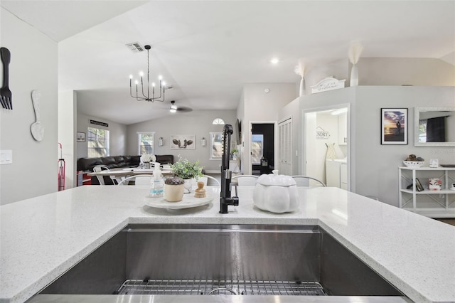 kitchen featuring lofted ceiling, an inviting chandelier, decorative light fixtures, and light stone counters