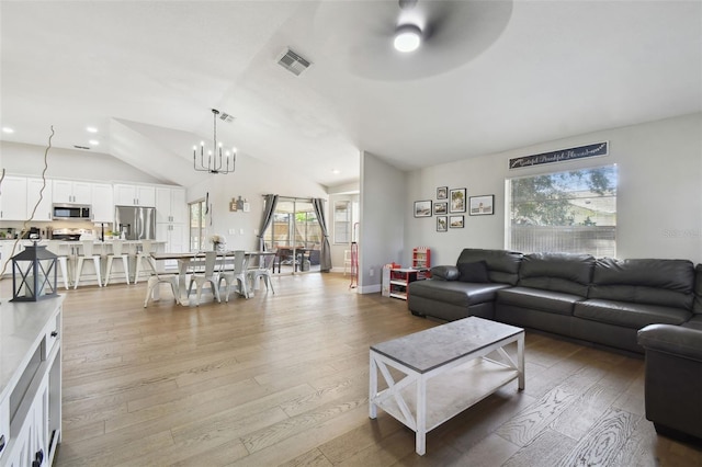 living room with ceiling fan with notable chandelier, lofted ceiling, a healthy amount of sunlight, and light wood-type flooring