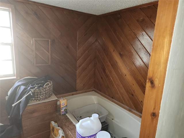 bathroom with a textured ceiling, a wealth of natural light, a bathing tub, and wood walls