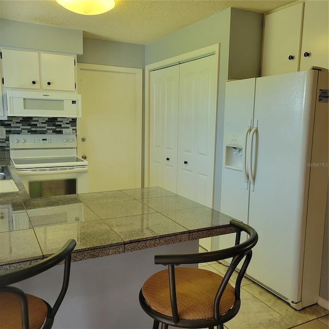 kitchen with white cabinets, light tile patterned floors, tasteful backsplash, white appliances, and a textured ceiling