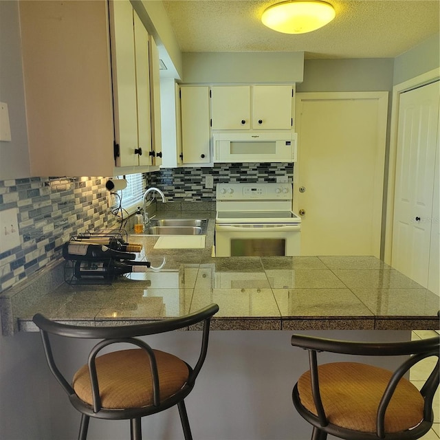 kitchen with white cabinetry, sink, white appliances, and a breakfast bar