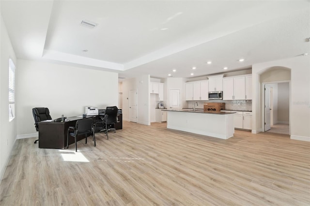 kitchen with white cabinetry, a tray ceiling, an island with sink, and light wood-type flooring