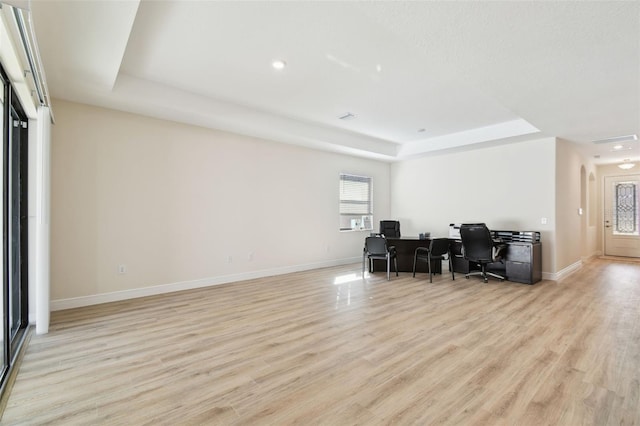 home office with light hardwood / wood-style floors and a raised ceiling