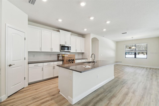 kitchen featuring sink, tasteful backsplash, an island with sink, pendant lighting, and white cabinets