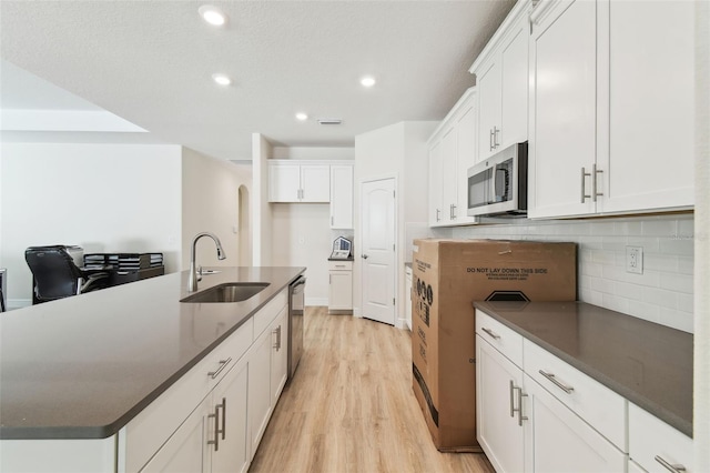 kitchen with appliances with stainless steel finishes, tasteful backsplash, sink, white cabinets, and a kitchen island with sink