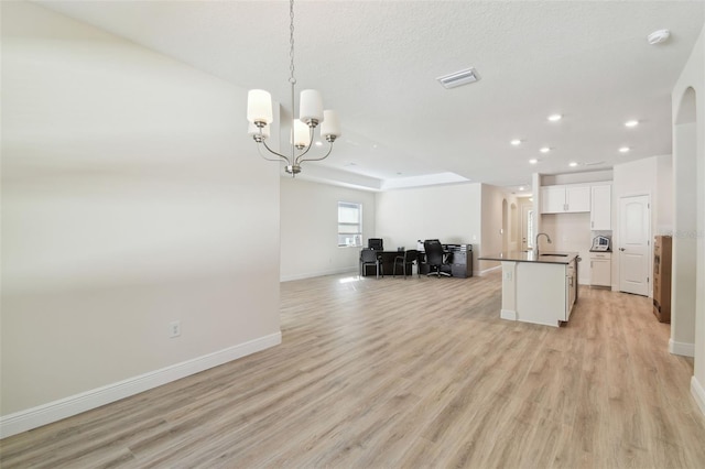 kitchen with sink, white cabinets, a kitchen island with sink, a notable chandelier, and light hardwood / wood-style floors