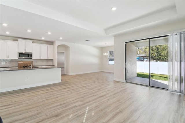 unfurnished living room featuring an inviting chandelier, a tray ceiling, and light wood-type flooring