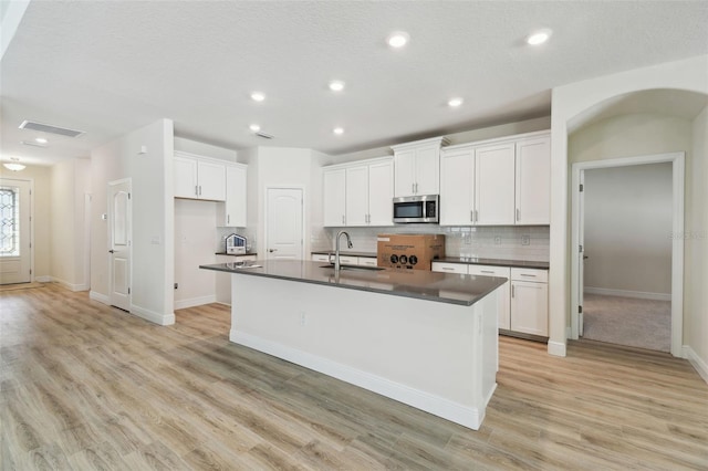 kitchen featuring tasteful backsplash, a kitchen island with sink, sink, and white cabinets