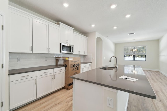 kitchen featuring sink, white cabinetry, an island with sink, decorative backsplash, and light wood-type flooring