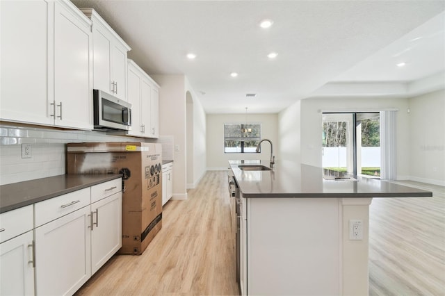 kitchen with an island with sink, sink, white cabinets, backsplash, and light hardwood / wood-style flooring