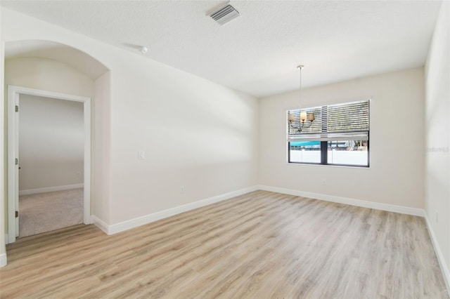 empty room with light hardwood / wood-style floors, a textured ceiling, and a notable chandelier