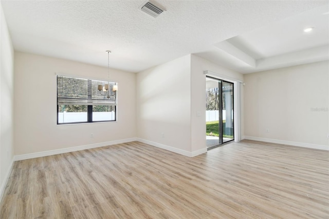 empty room with plenty of natural light, a textured ceiling, and light hardwood / wood-style floors