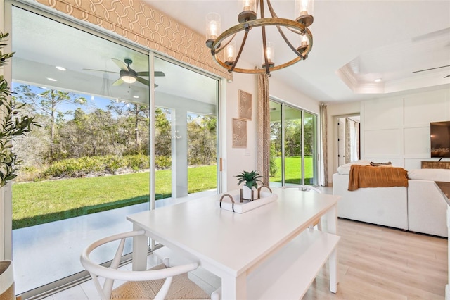 sunroom featuring a raised ceiling, ceiling fan with notable chandelier, and a healthy amount of sunlight