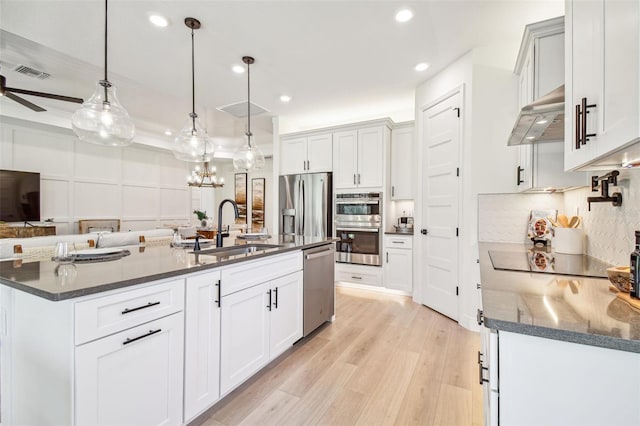 kitchen featuring a kitchen island with sink, decorative light fixtures, exhaust hood, stainless steel appliances, and light wood-type flooring