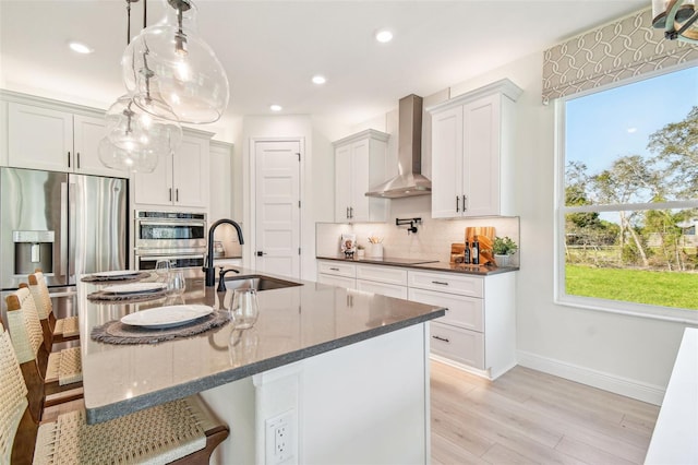 kitchen featuring sink, wall chimney exhaust hood, white cabinetry, appliances with stainless steel finishes, and light wood-type flooring