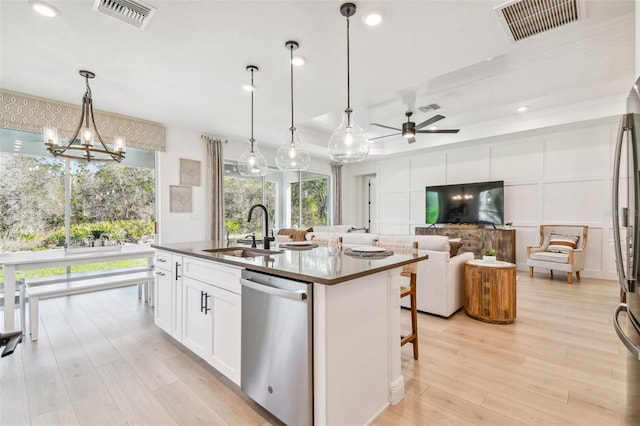 kitchen with a kitchen island with sink, stainless steel dishwasher, sink, white cabinetry, and decorative light fixtures