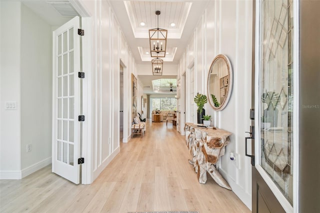 hallway with light hardwood / wood-style flooring, a chandelier, a raised ceiling, crown molding, and french doors