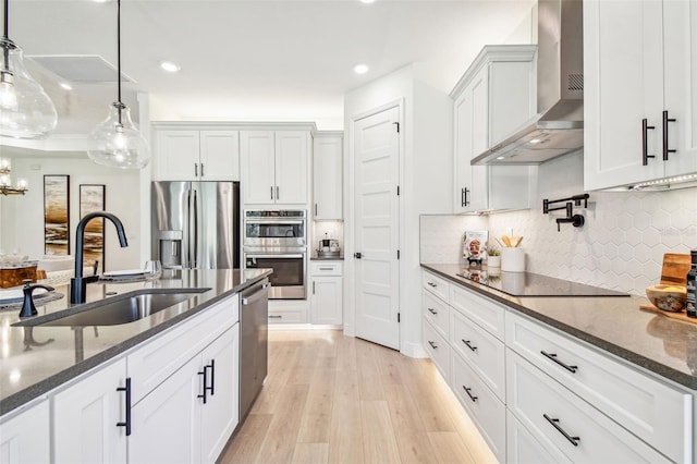 kitchen featuring stainless steel appliances, wall chimney range hood, pendant lighting, and white cabinetry