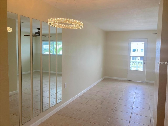 empty room featuring ceiling fan with notable chandelier and light tile patterned floors