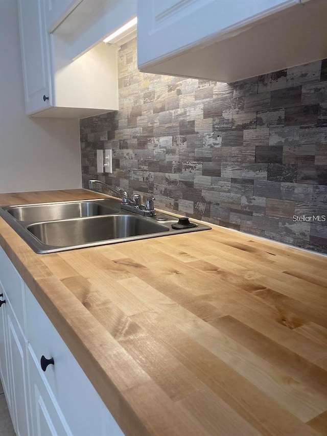 kitchen featuring decorative backsplash, white cabinetry, sink, and wood counters