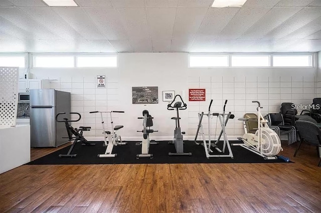 workout area with tile walls, dark hardwood / wood-style flooring, and a healthy amount of sunlight