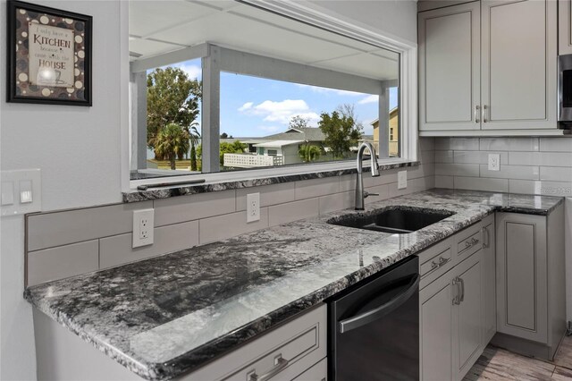 kitchen featuring dishwashing machine, light stone counters, backsplash, and a sink