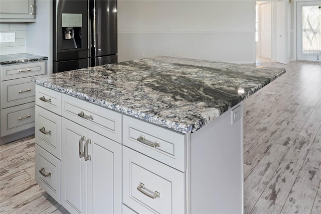 kitchen with tasteful backsplash, light hardwood / wood-style floors, stainless steel fridge with ice dispenser, and stone countertops