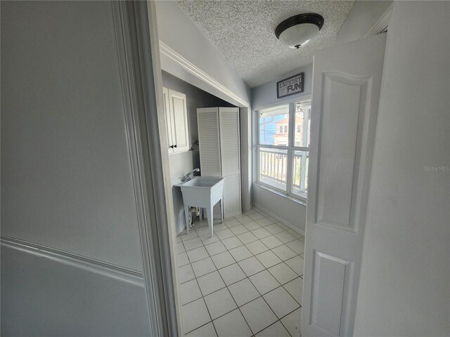 hallway featuring baseboards, a textured ceiling, and light tile patterned floors