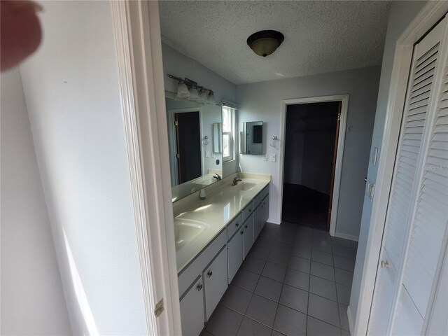 bathroom with double vanity, a sink, a textured ceiling, and tile patterned floors