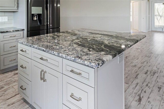 kitchen featuring light wood-style floors, a center island, stone countertops, and black fridge with ice dispenser