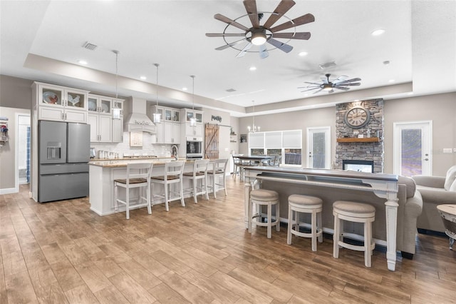 kitchen with decorative light fixtures, white cabinetry, stainless steel appliances, custom range hood, and light hardwood / wood-style floors