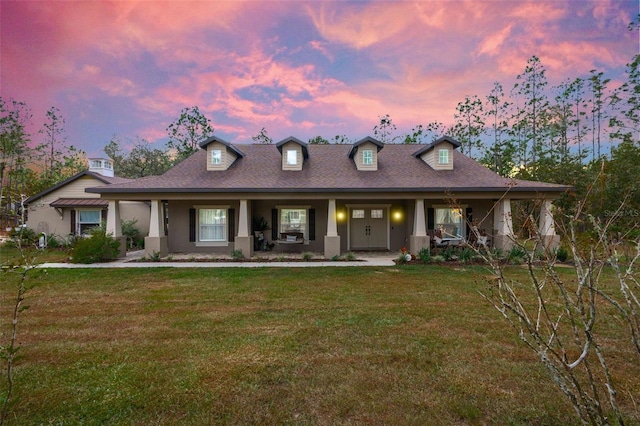 cape cod-style house featuring a lawn and covered porch