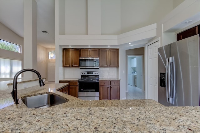 kitchen featuring light stone counters, sink, a high ceiling, and appliances with stainless steel finishes