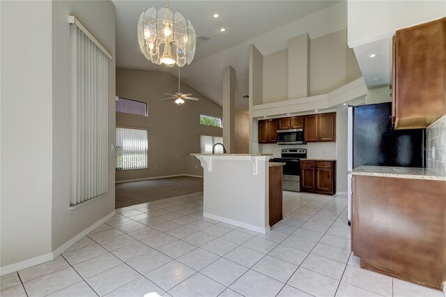 kitchen featuring a breakfast bar, ceiling fan with notable chandelier, stainless steel appliances, and light tile patterned flooring