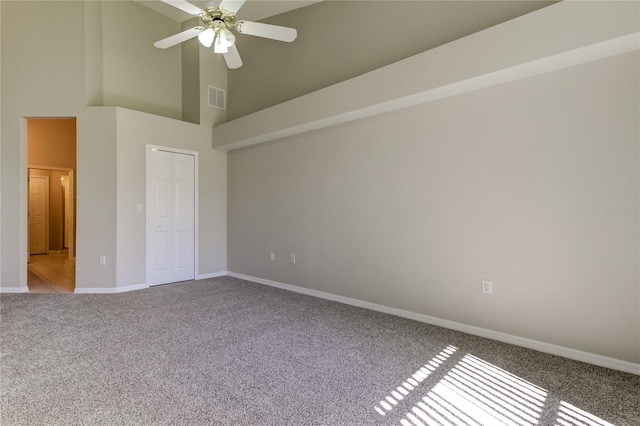 empty room featuring ceiling fan, light colored carpet, and a high ceiling