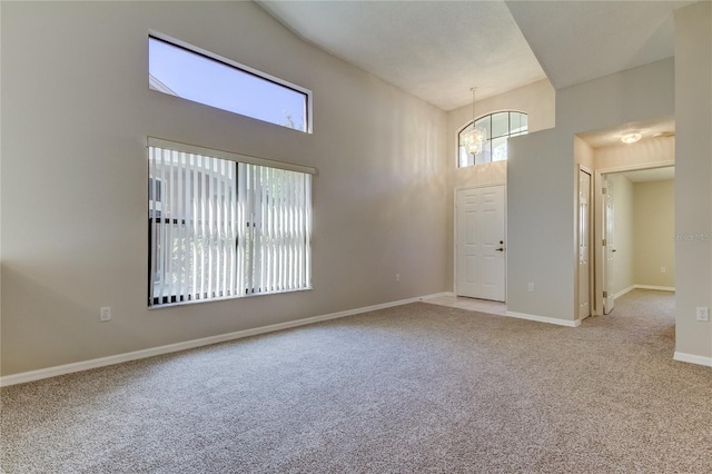 spare room with a high ceiling, light colored carpet, and a notable chandelier