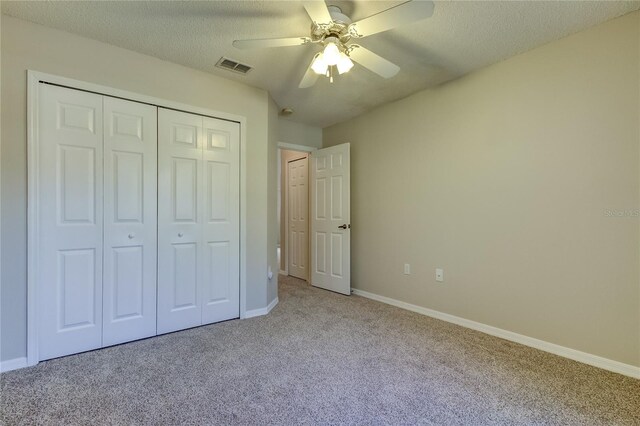 unfurnished bedroom with a textured ceiling, ceiling fan, light carpet, and a closet