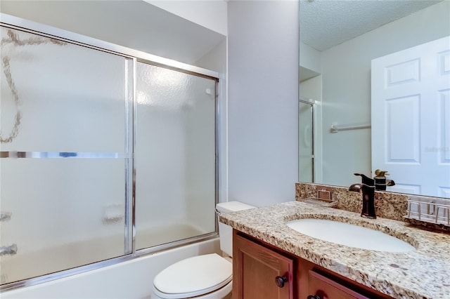 full bathroom with vanity, bath / shower combo with glass door, a textured ceiling, and toilet