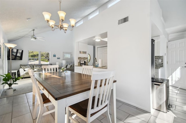 tiled dining room featuring high vaulted ceiling, ceiling fan with notable chandelier, sink, a fireplace, and a textured ceiling