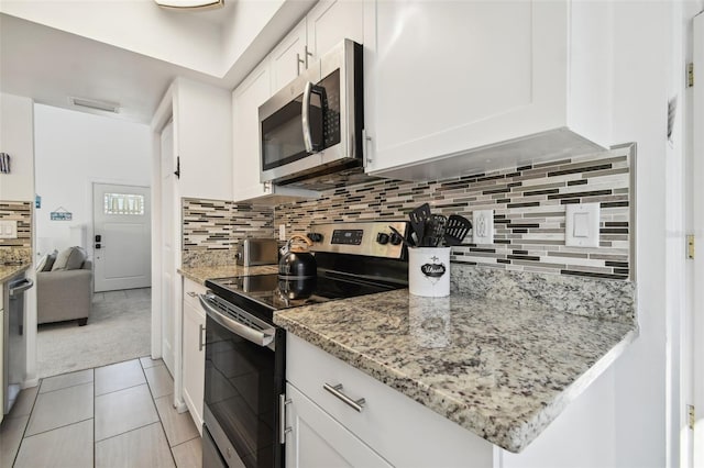 kitchen featuring white cabinetry, tasteful backsplash, light stone counters, light tile patterned floors, and appliances with stainless steel finishes