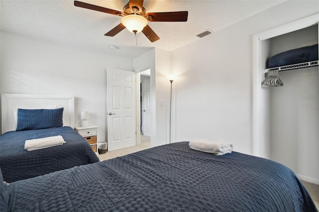 bedroom with ceiling fan, light colored carpet, a textured ceiling, and a closet