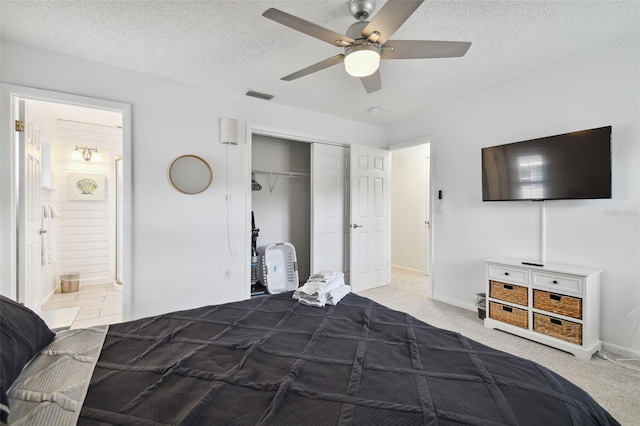 bedroom with light carpet, ceiling fan, a textured ceiling, connected bathroom, and a closet