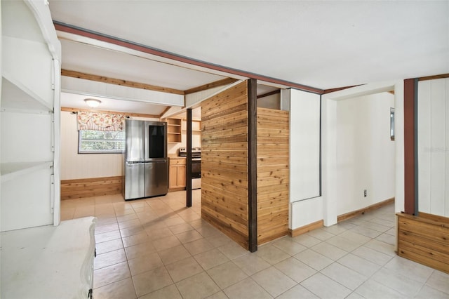 interior space with wood walls, stainless steel refrigerator, light tile patterned flooring, and electric range