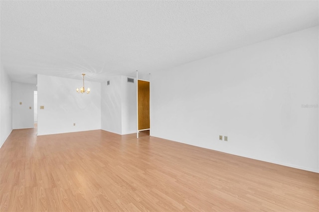 spare room with a chandelier, light hardwood / wood-style flooring, and a textured ceiling