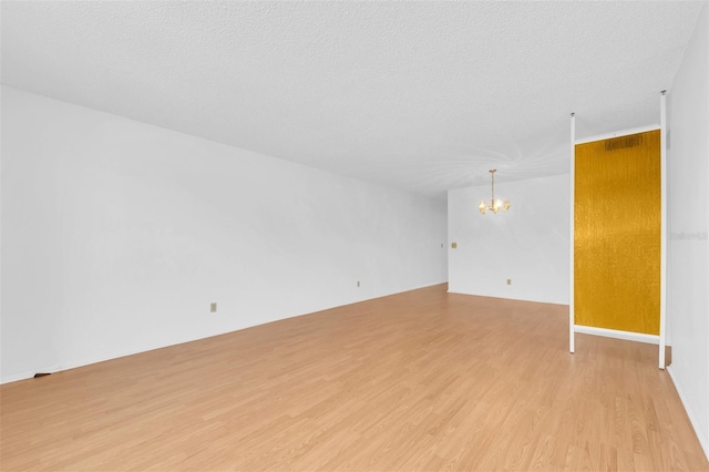 spare room featuring an inviting chandelier, light hardwood / wood-style flooring, and a textured ceiling