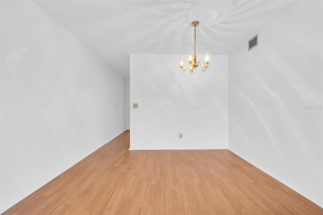 unfurnished room with a notable chandelier and light wood-type flooring