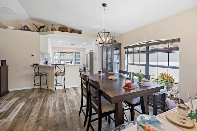 dining space featuring wood-type flooring, an inviting chandelier, lofted ceiling, and a water view