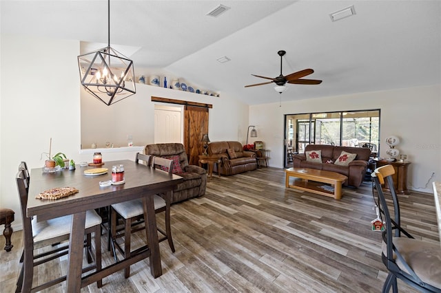 dining area with vaulted ceiling, ceiling fan with notable chandelier, hardwood / wood-style floors, and a barn door