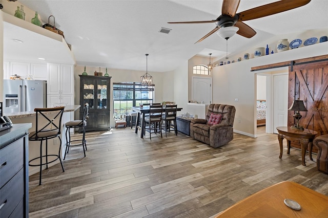 living room featuring lofted ceiling, ceiling fan, a barn door, and wood-type flooring