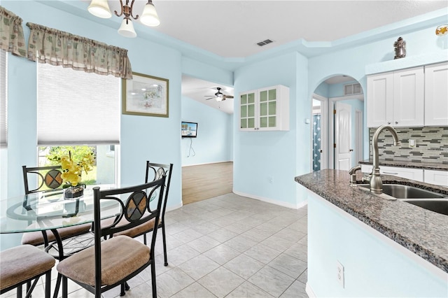 kitchen featuring decorative backsplash, white cabinets, ceiling fan, dark stone countertops, and sink